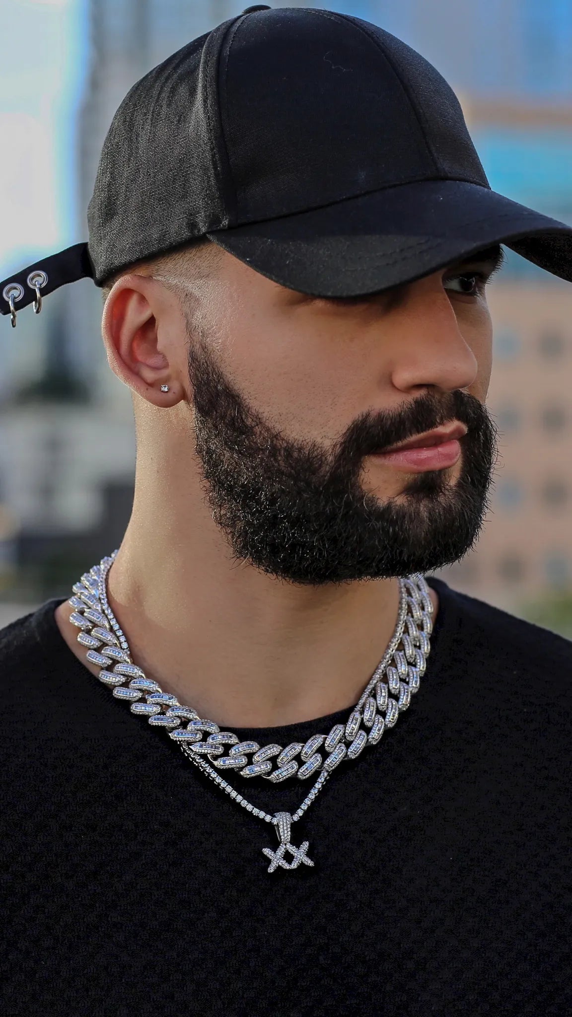 Man wearing a black cap and silver chain necklace with a blurred background