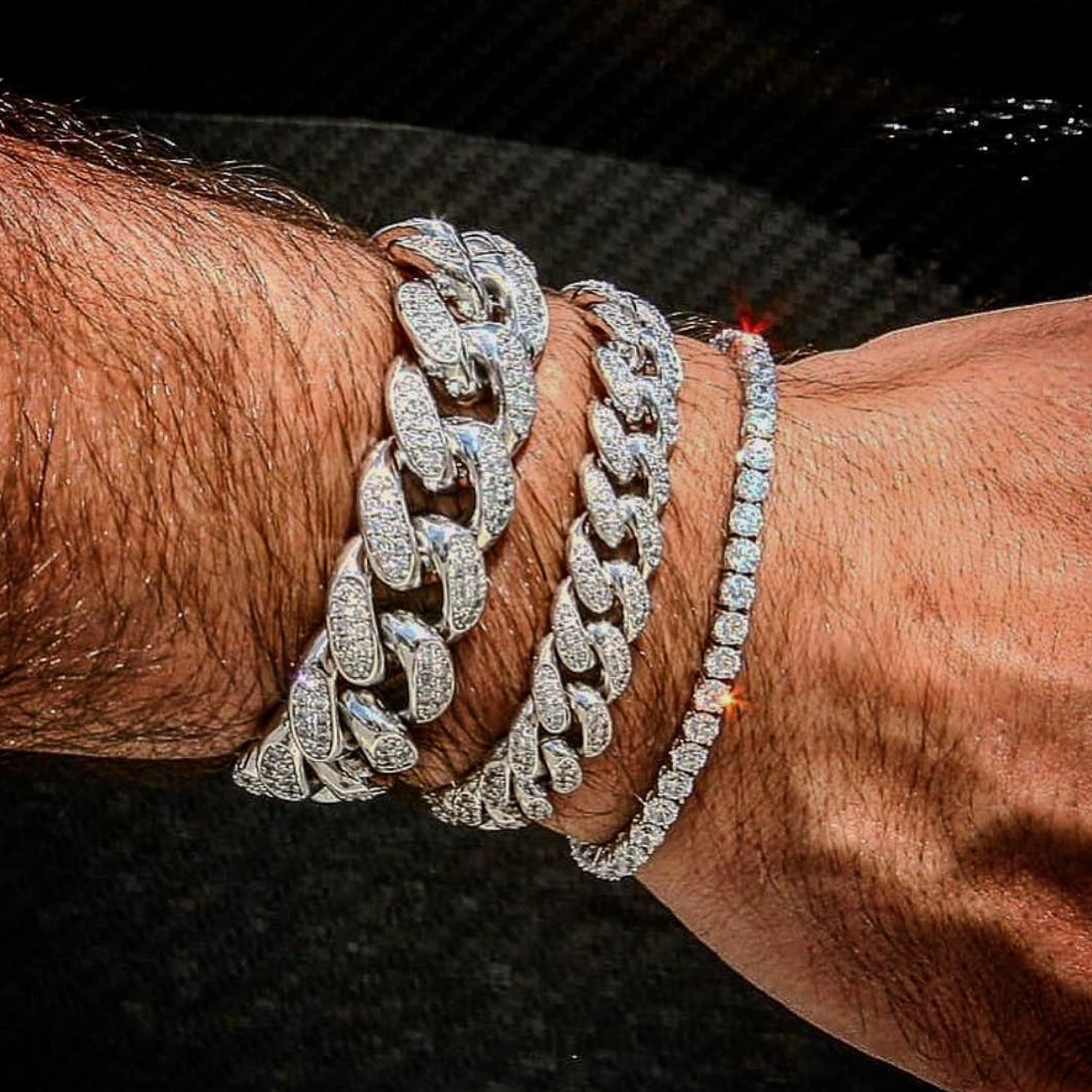 Close-up of a wrist wearing two silver chain bracelets with diamond accents on a dark background.
