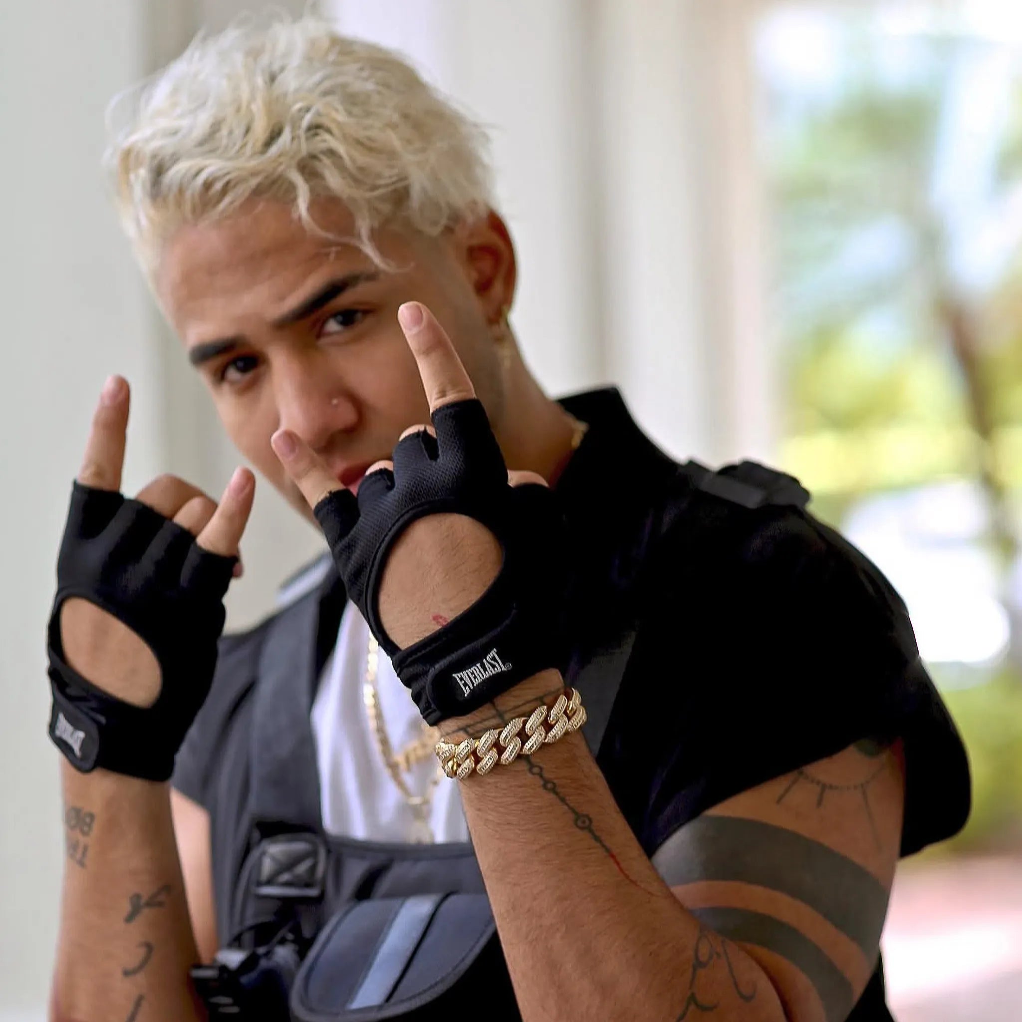 Person wearing black gloves and gold bracelets with a blurred outdoor background