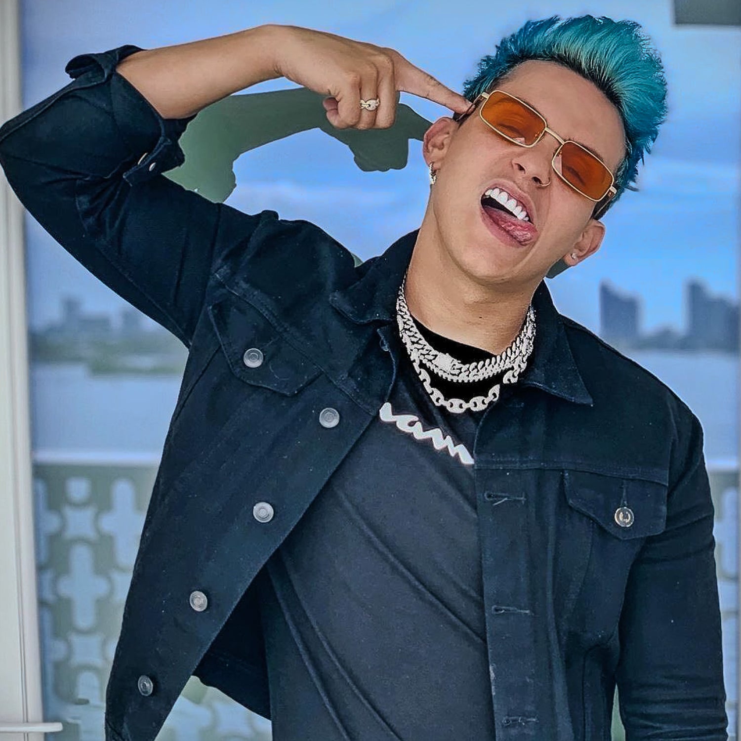 Person with blue hair and sunglasses posing in front of a blurred background