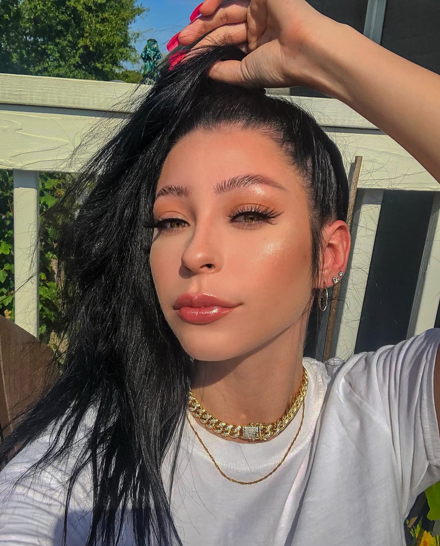 Person with styled hair outdoors, wearing a white shirt and gold necklace
