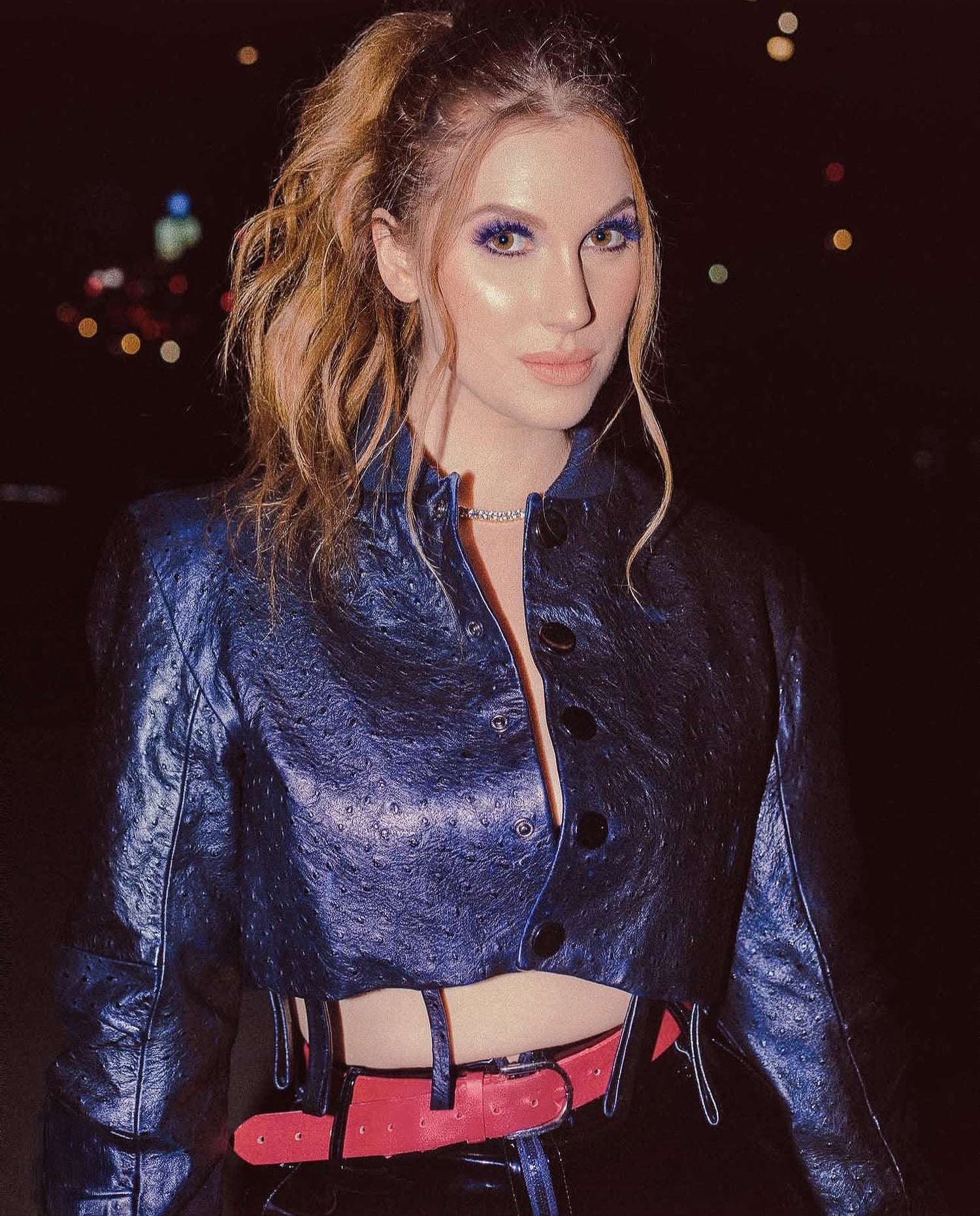 Person wearing a blue textured outfit with a red belt against a dark background