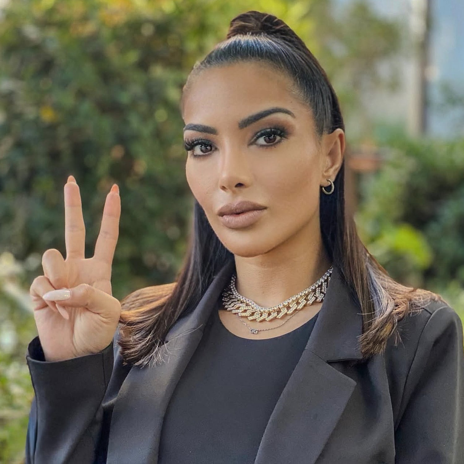 Woman making a peace sign outdoors with greenery in the background