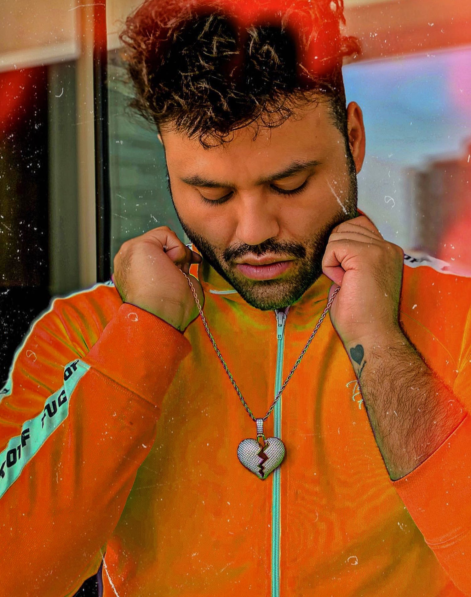 Person wearing an orange jacket with a heart-shaped pendant, standing indoors.