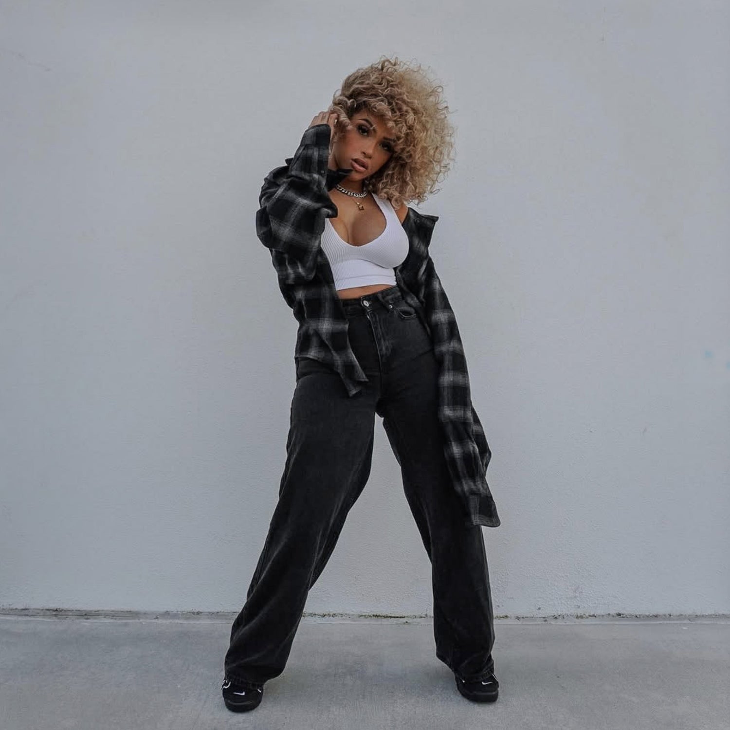 Woman wearing a plaid shirt over a white top and black pants against a plain background