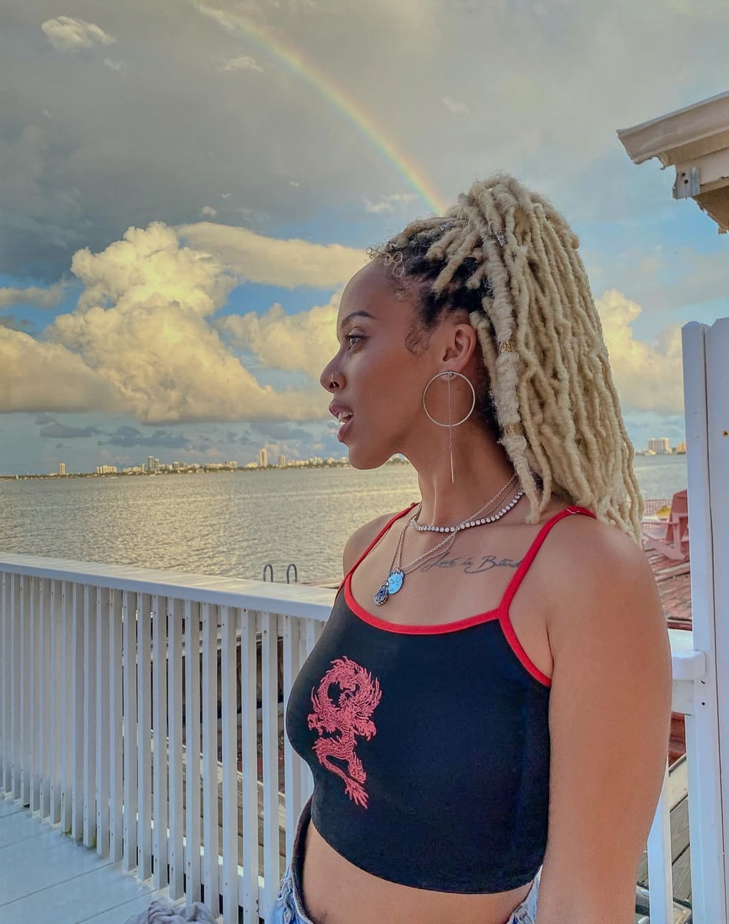 Woman with braided hair standing on a balcony with a rainbow and city skyline in the background