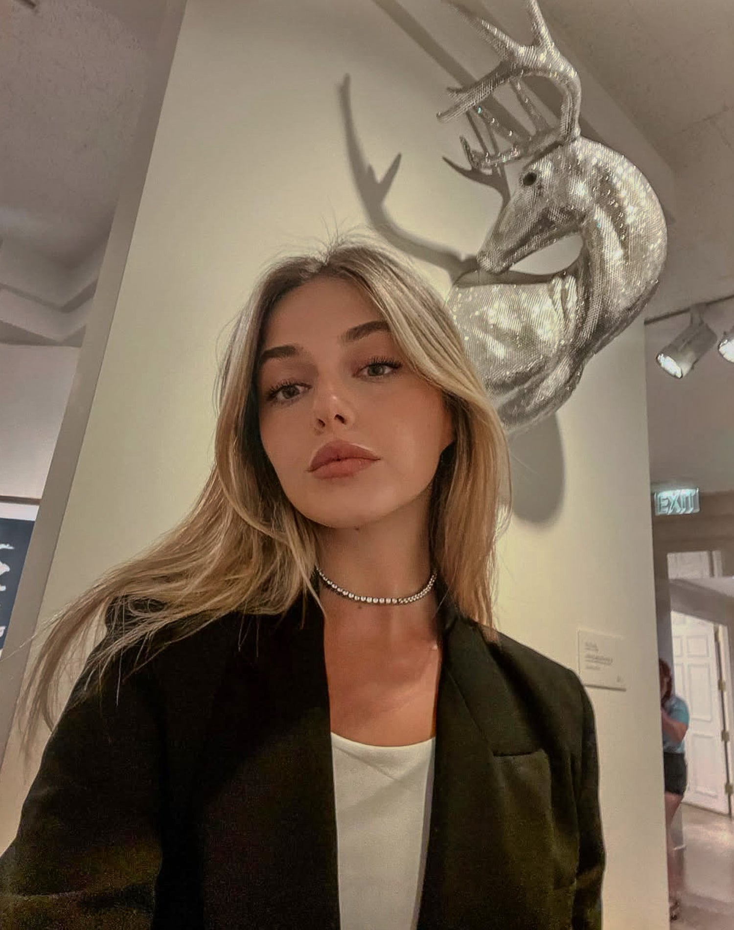 Woman posing in front of a decorative deer head sculpture in an indoor setting