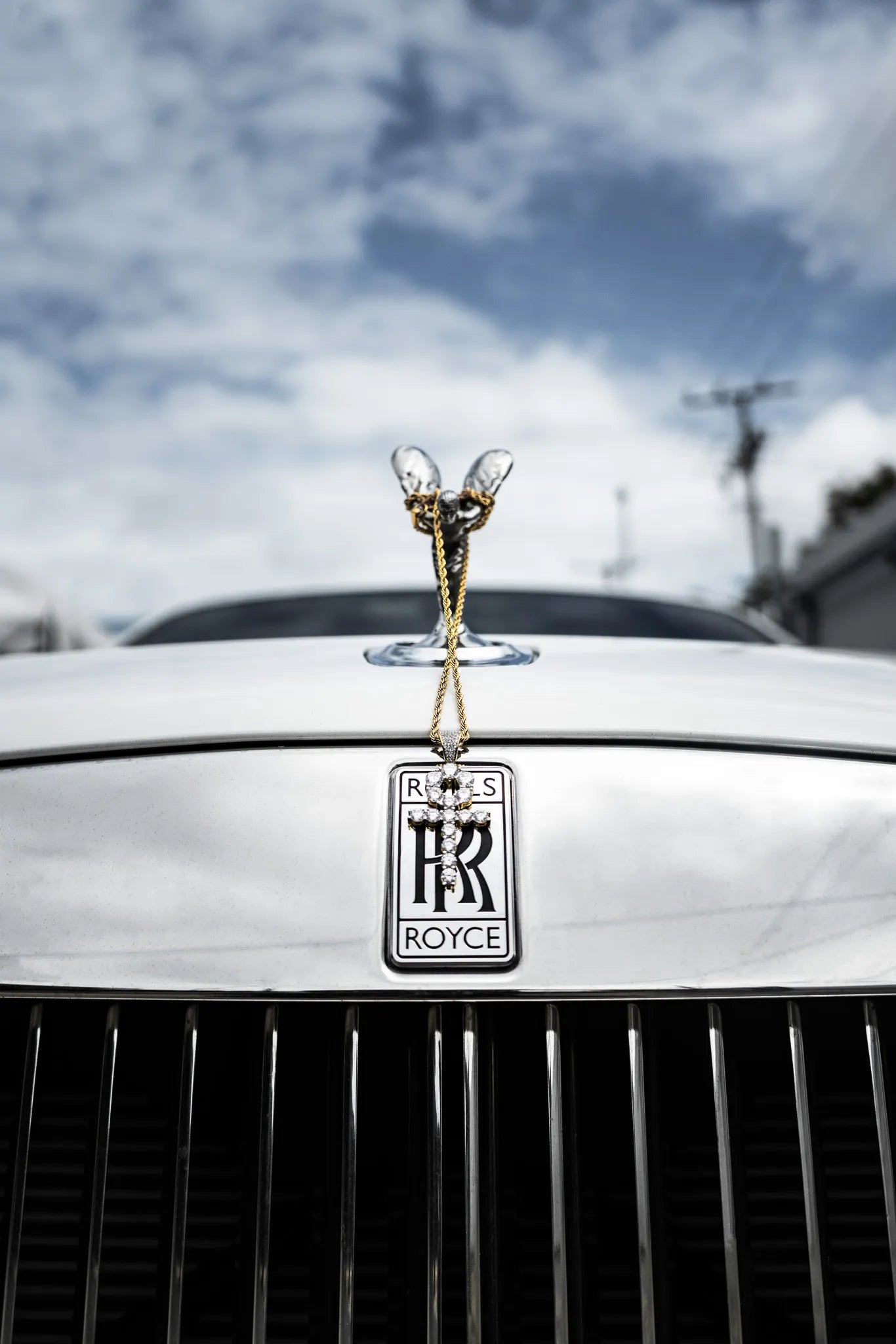 Rolls-Royce car emblem with a gold angel on a white car against a cloudy sky.
